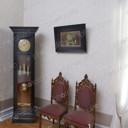 A grandfather clock and two chairs in a room in a hotel.