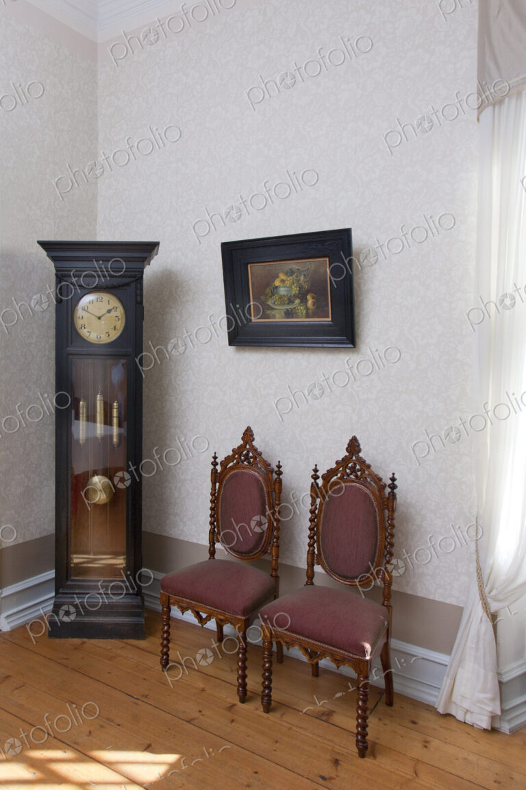 A grandfather clock and two chairs in a room in a hotel.