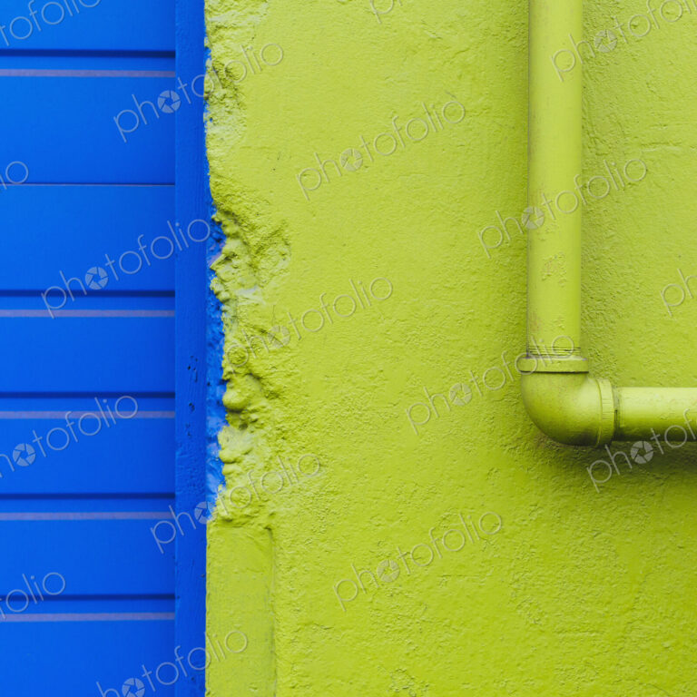 A green painted wall and pipe by a blue doorway.