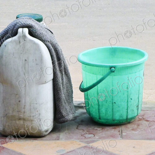 A green plastic bucket and a container of liquid with a cloth, on the sidewalk in New…