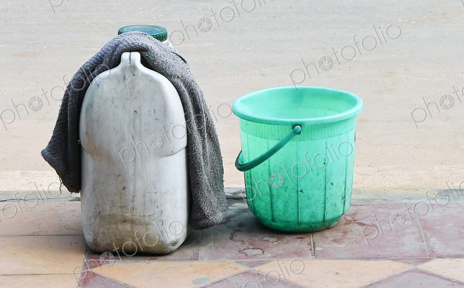 A green plastic bucket and a container of liquid with a cloth, on the sidewalk in New…
