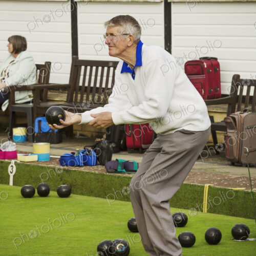 A grey haired man standing on a yellow mat on a lawn bowls green, bending his knees… A grey haired man standing on a yellow mat on a lawn bowls green, bending his knees…