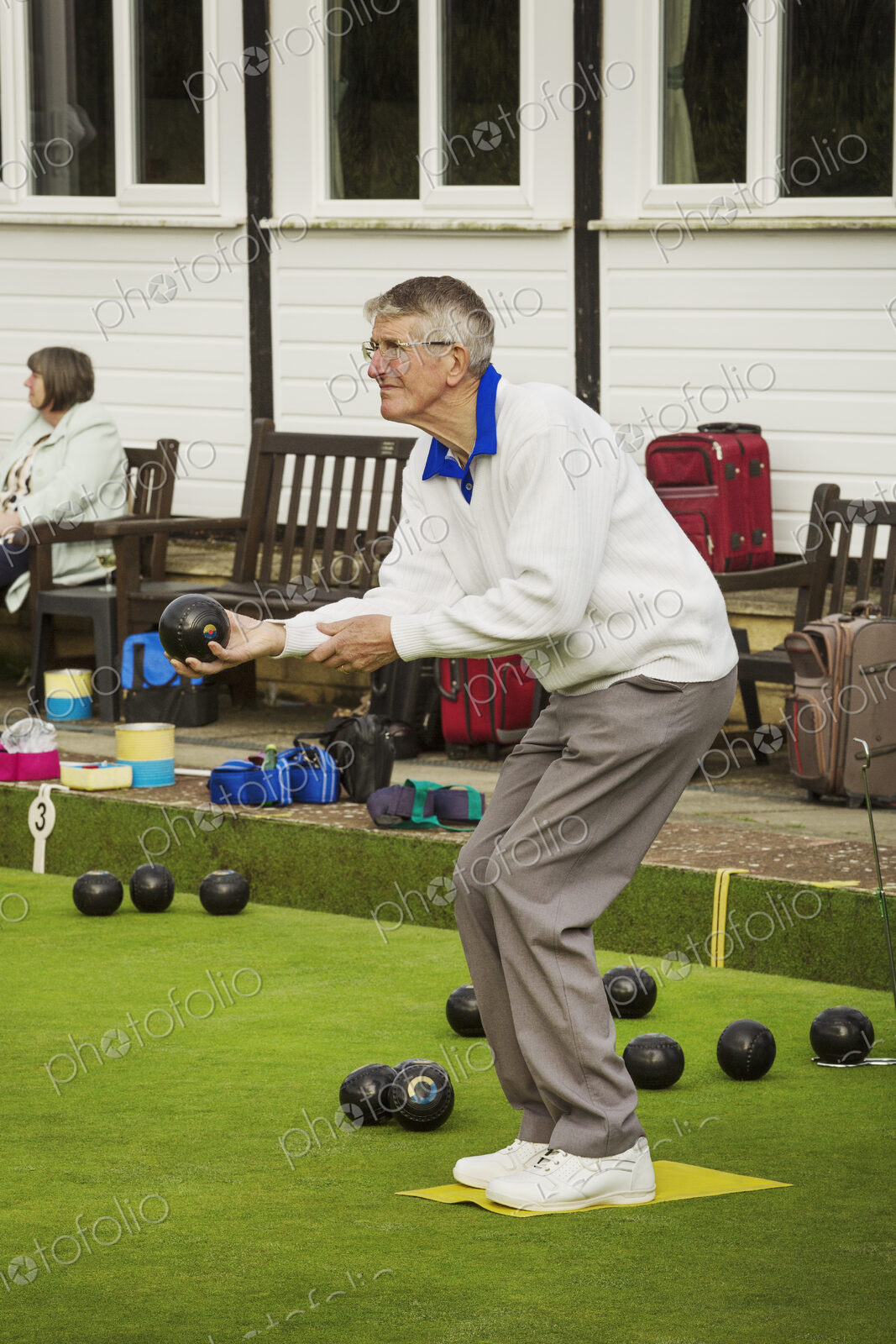 A grey haired man standing on a yellow mat on a lawn bowls green, bending his knees…