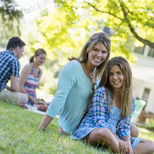 A group of adults and children sitting on the grass under the shade of a tree. A… A group of adults and children sitting on the grass under the shade of a tree. A…