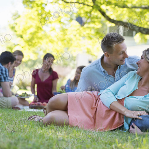 A group of adults and children sitting on the grass under the shade of a tree. A… A group of adults and children sitting on the grass under the shade of a tree. A…
