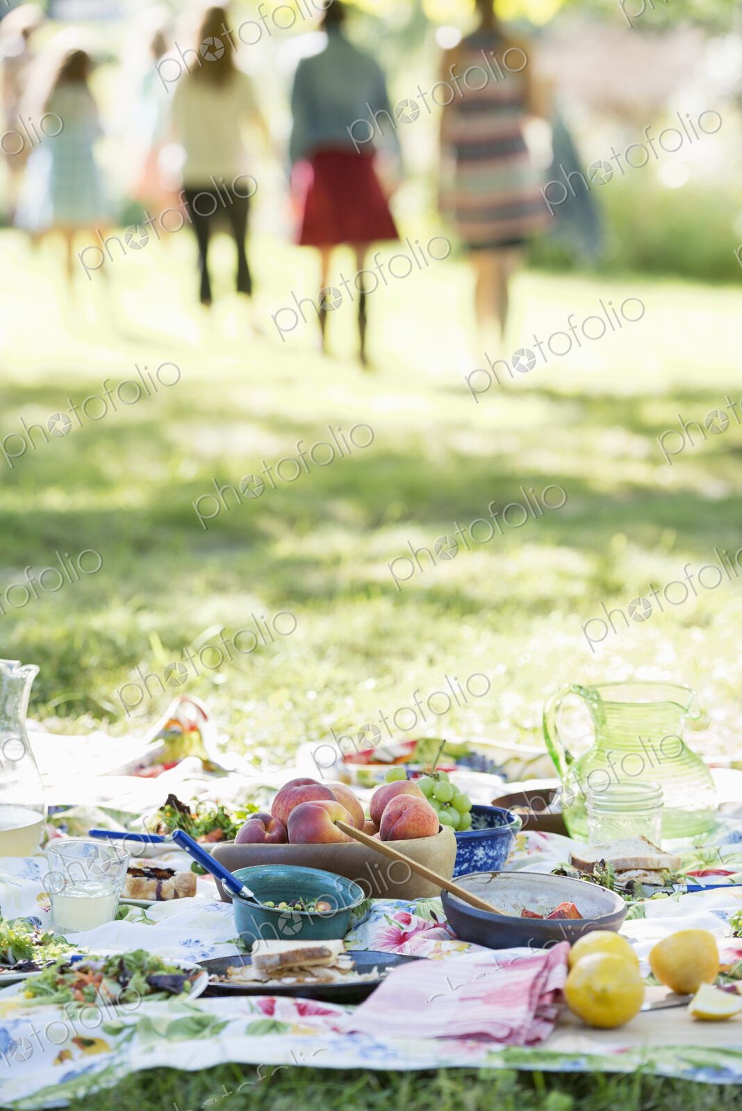 A group of adults and children sitting on the grass under the shade of a tree. A…