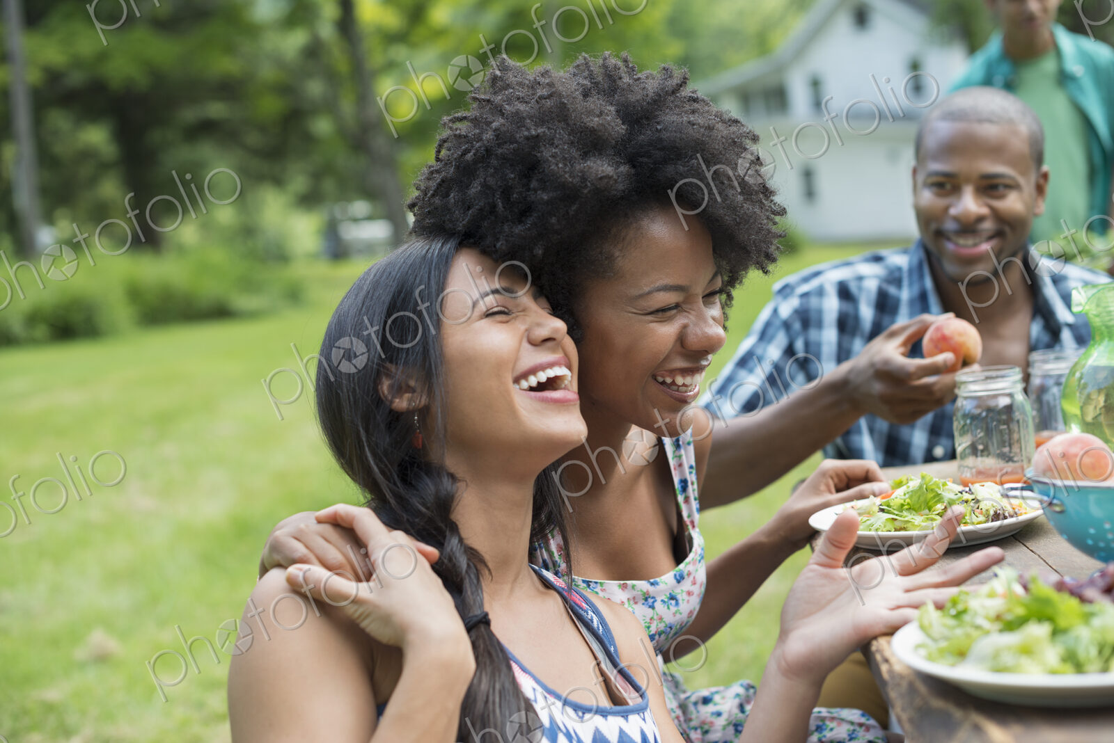 A group of adults and young people at a meal in the garden of a farmhouse. Passing…