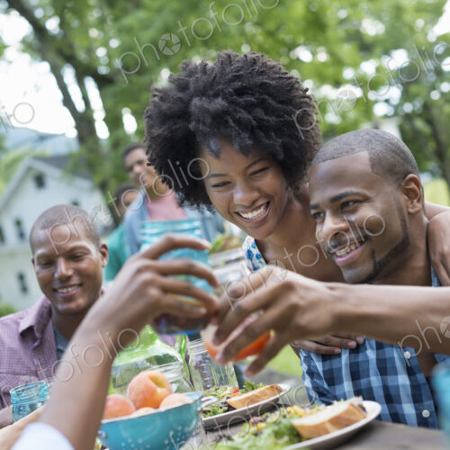 A group of adults and young people at a meal in the garden of a farmhouse. Passing…