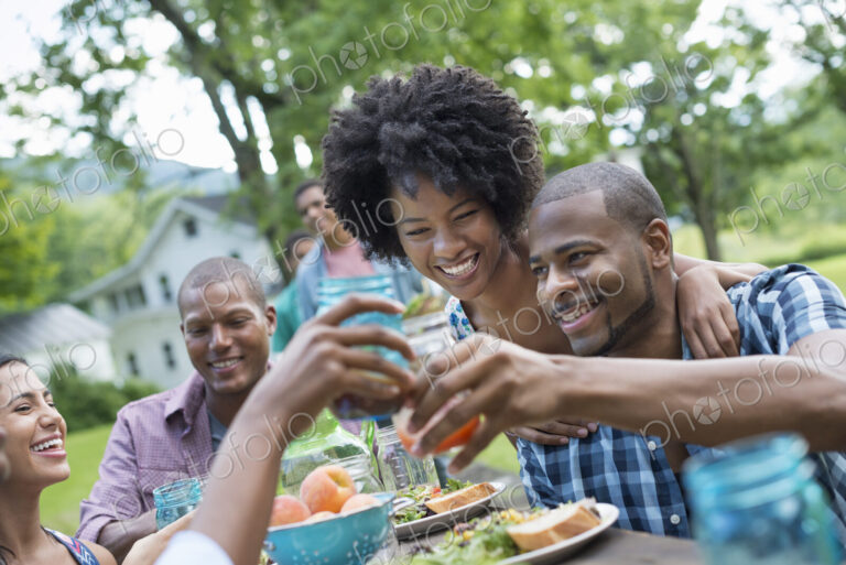 A group of adults and young people at a meal in the garden of a farmhouse. Passing…