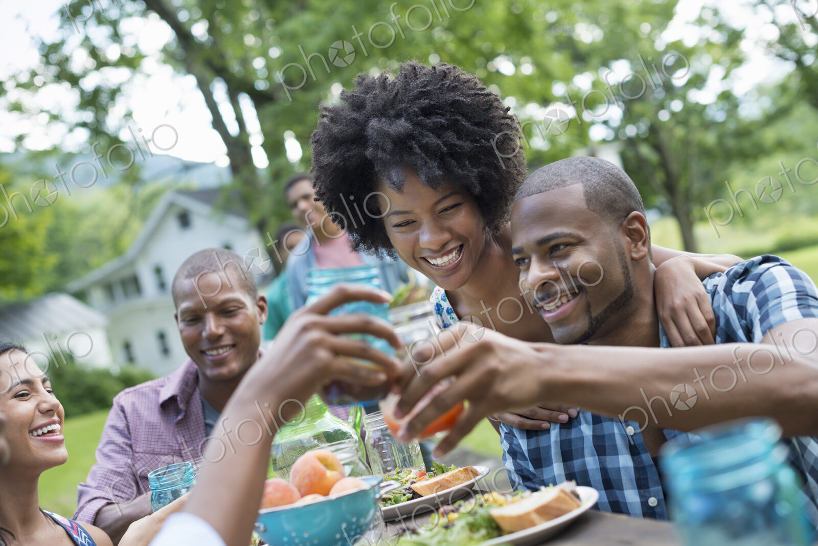 A group of adults and young people at a meal in the garden of a farmhouse. Passing…