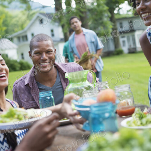 A group of adults and young people at a meal in the garden of a farmhouse. Passing…