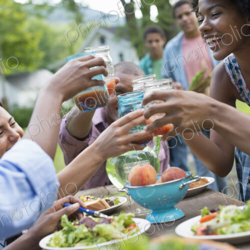 A group of adults and young people at a meal in the garden of a farmhouse. Passing…