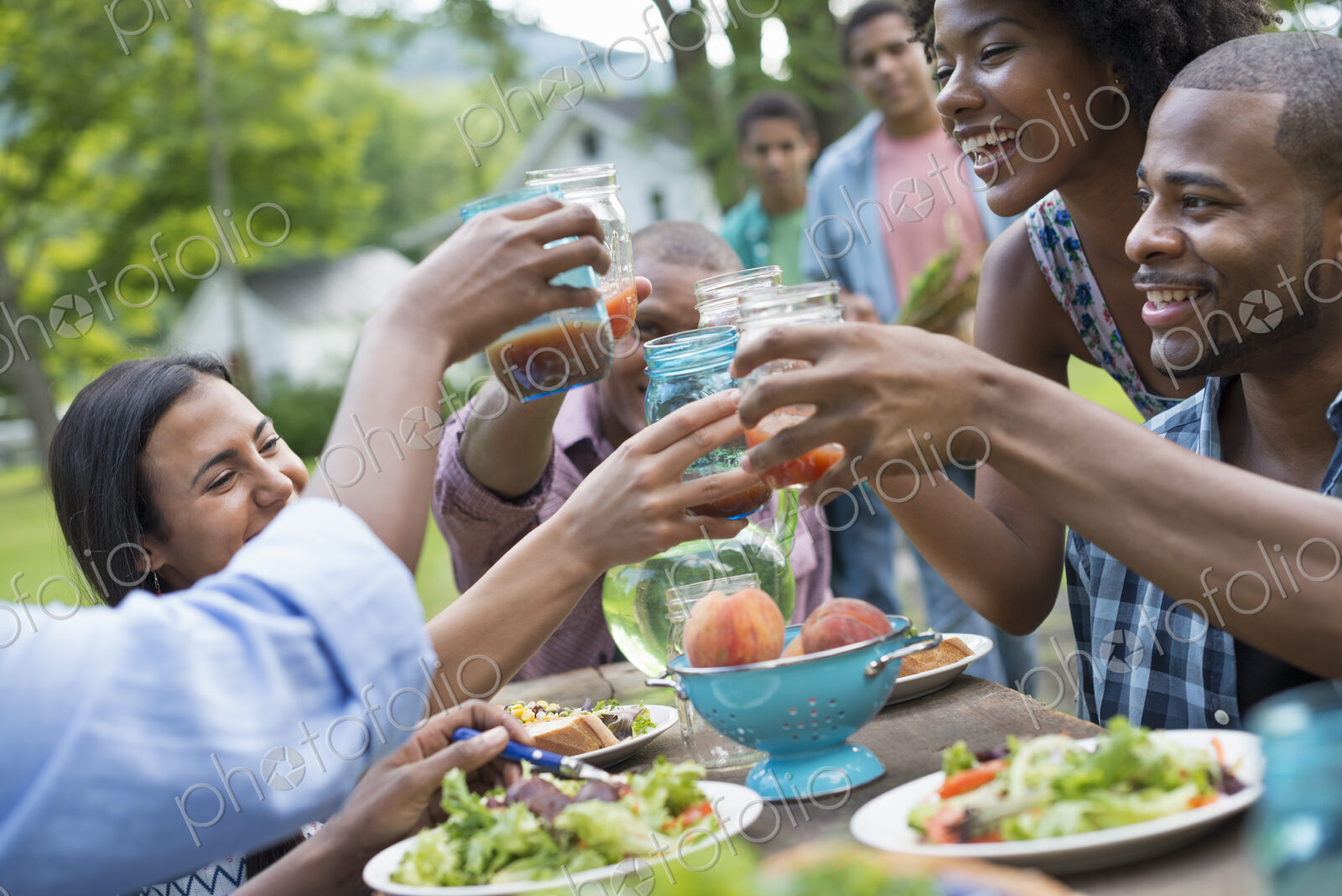 A group of adults and young people at a meal in the garden of a farmhouse. Passing…