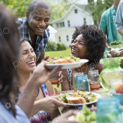 A group of adults and young people at a meal in the garden of a farmhouse. Passing…