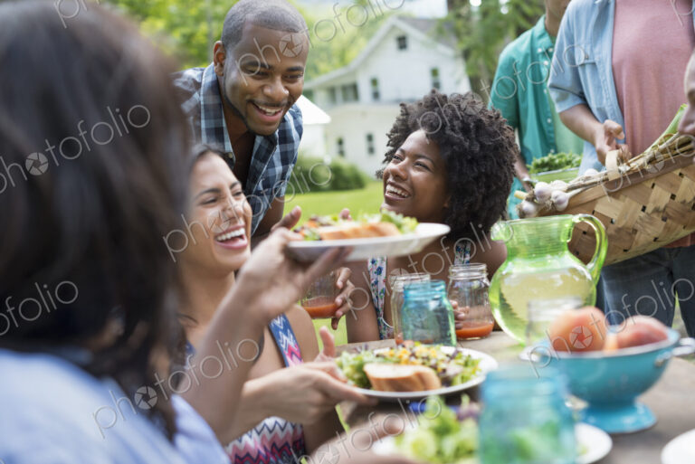 A group of adults and young people at a meal in the garden of a farmhouse. Passing…
