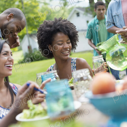 A group of adults and young people at a meal in the garden of a farmhouse. Passing…