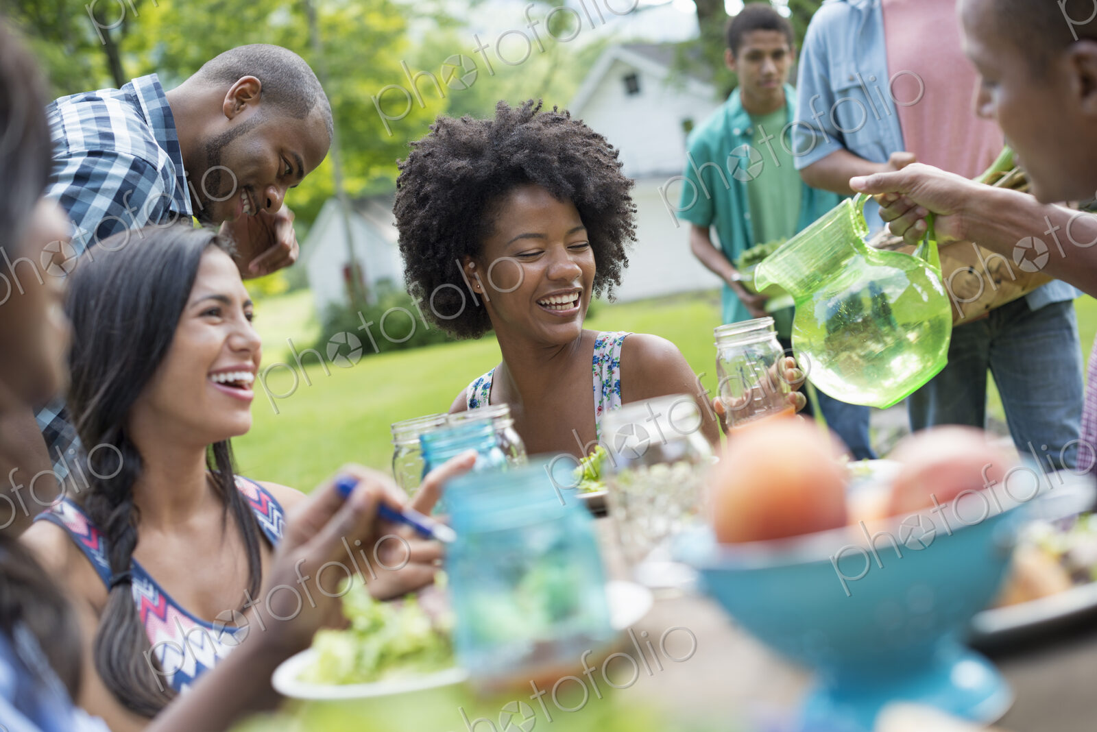 A group of adults and young people at a meal in the garden of a farmhouse. Passing…