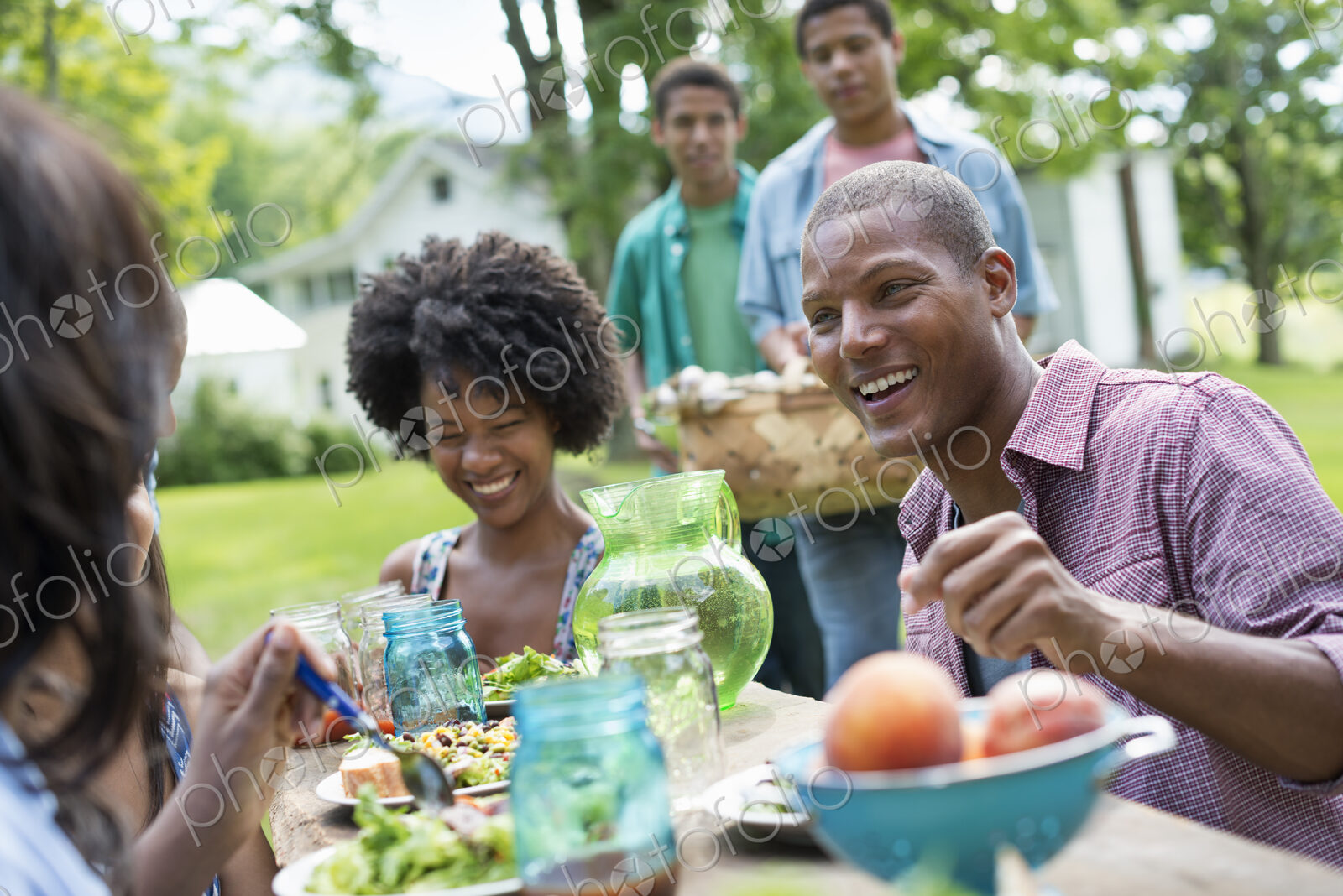 A group of adults and young people at a meal in the garden of a farmhouse. Passing…