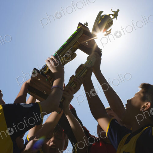 A group of boys in soccer team shirts holding a trophy and celebrating a win. A group of boys in soccer team shirts holding a trophy and celebrating a win.