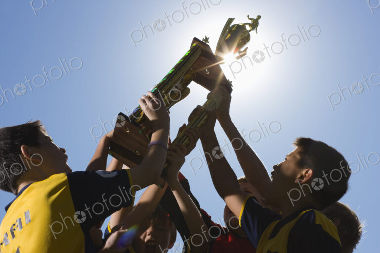 A group of boys in soccer team shirts holding a trophy and celebrating a win.