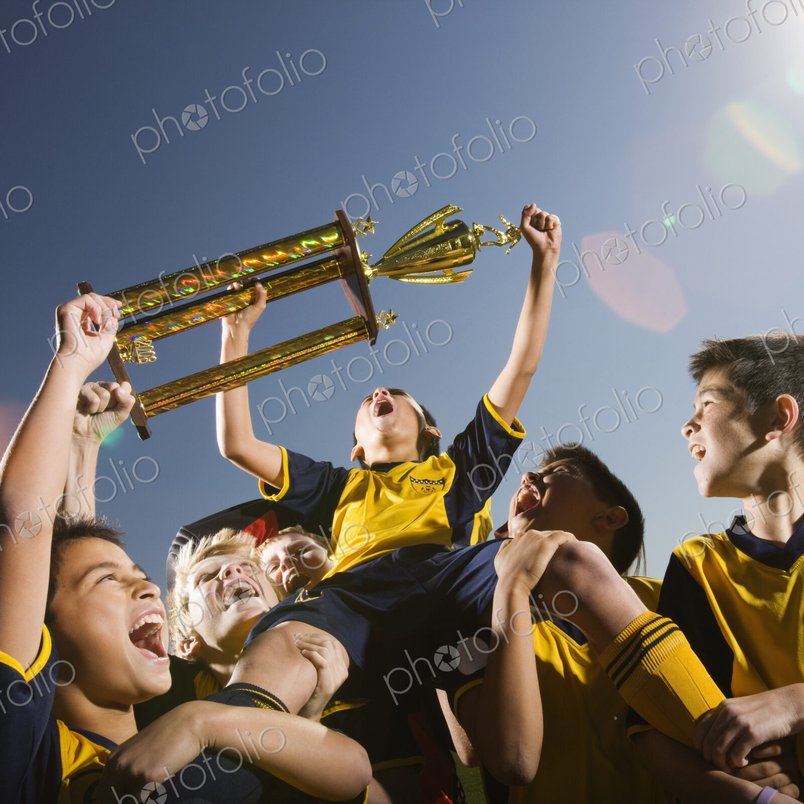 A group of boys in soccer team shirts holding a trophy and celebrating a win.