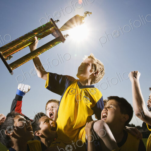 A group of boys in soccer team shirts holding a trophy and celebrating a win. A group of boys in soccer team shirts holding a trophy and celebrating a win.