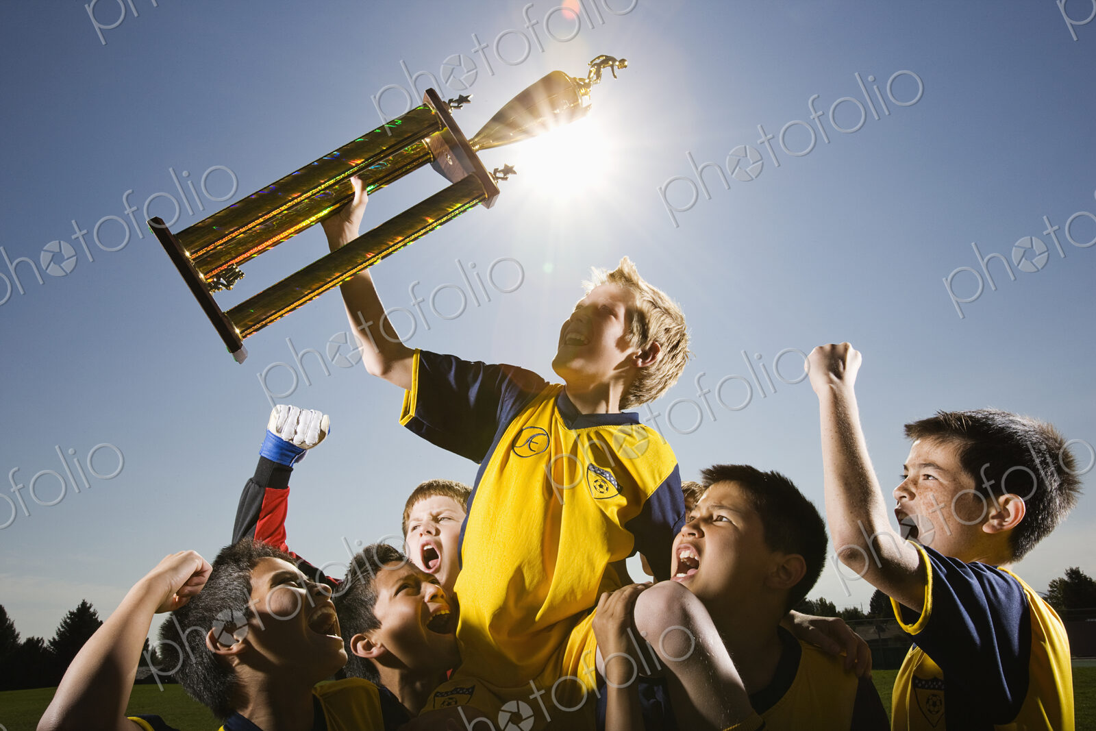 A group of boys in soccer team shirts holding a trophy and celebrating a win.