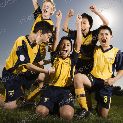 A group of boys in soccer team shirts holding a trophy and celebrating a win. A group of boys in soccer team shirts holding a trophy and celebrating a win.