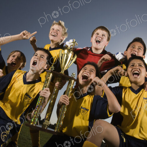 A group of boys in soccer team shirts holding a trophy and celebrating a win. A group of boys in soccer team shirts holding a trophy and celebrating a win.