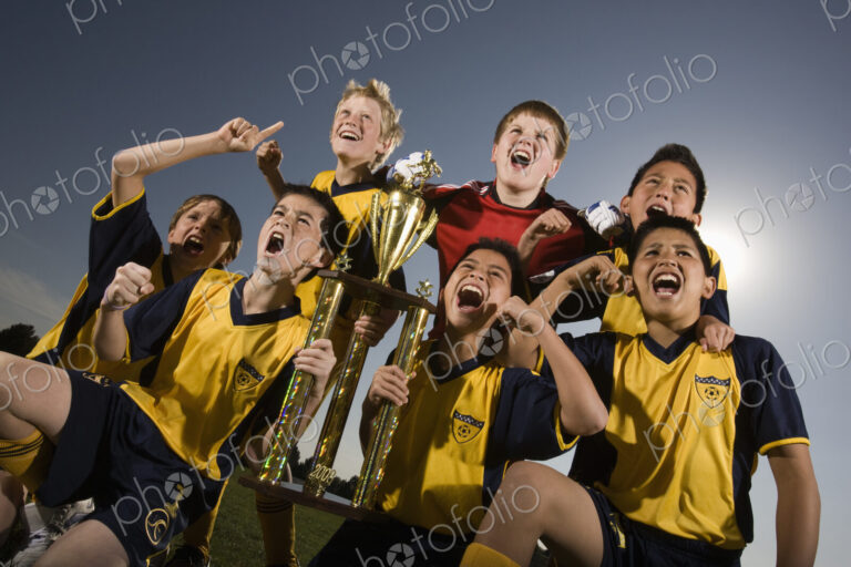 A group of boys in soccer team shirts holding a trophy and celebrating a win.