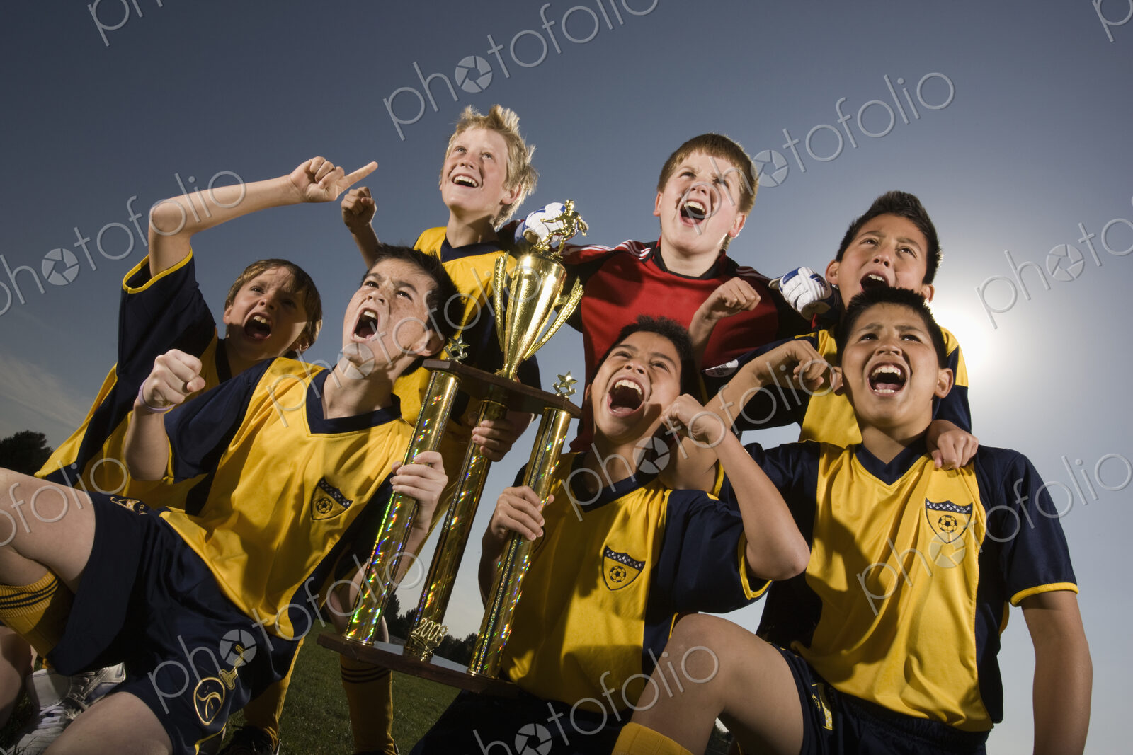 A group of boys in soccer team shirts holding a trophy and celebrating a win.