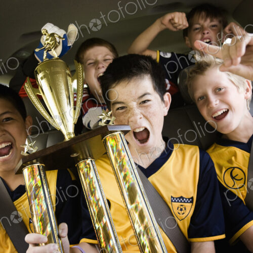 A group of boys in soccer team shirts holding a trophy and celebrating a win. In a… A group of boys in soccer team shirts holding a trophy and celebrating a win. In a…
