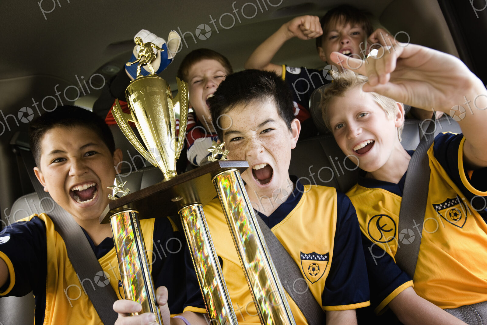 A group of boys in soccer team shirts holding a trophy and celebrating a win. In a…