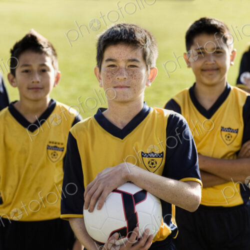 A group of boys in team football shirts, one holding a soccer ball.