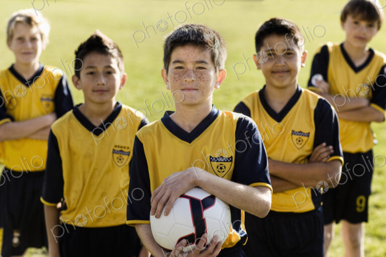 A group of boys in team football shirts, one holding a soccer ball.