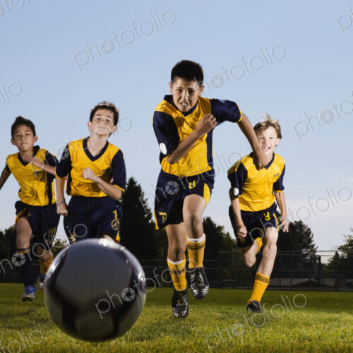 A group of boys running towards a soocer ball.