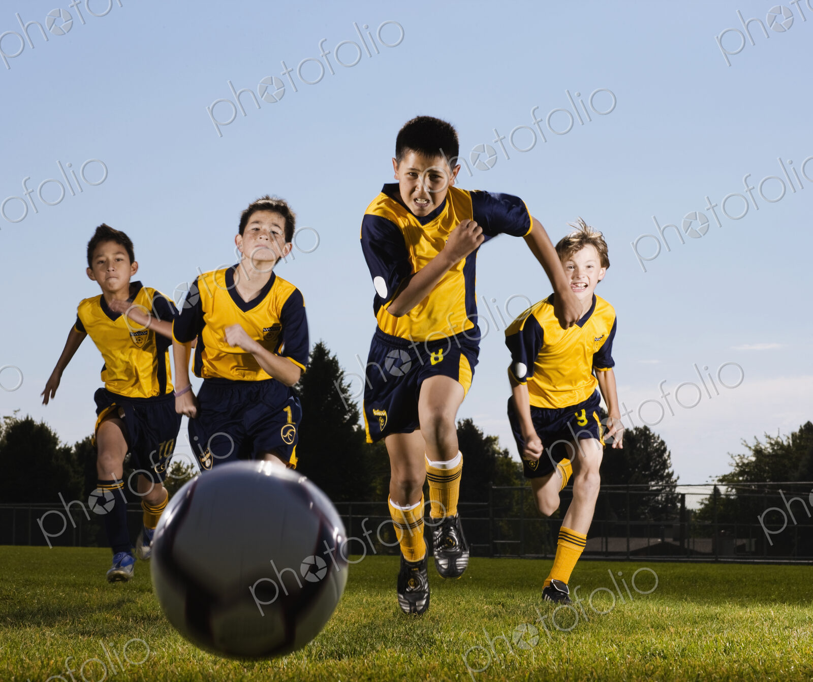 A group of boys running towards a soocer ball.