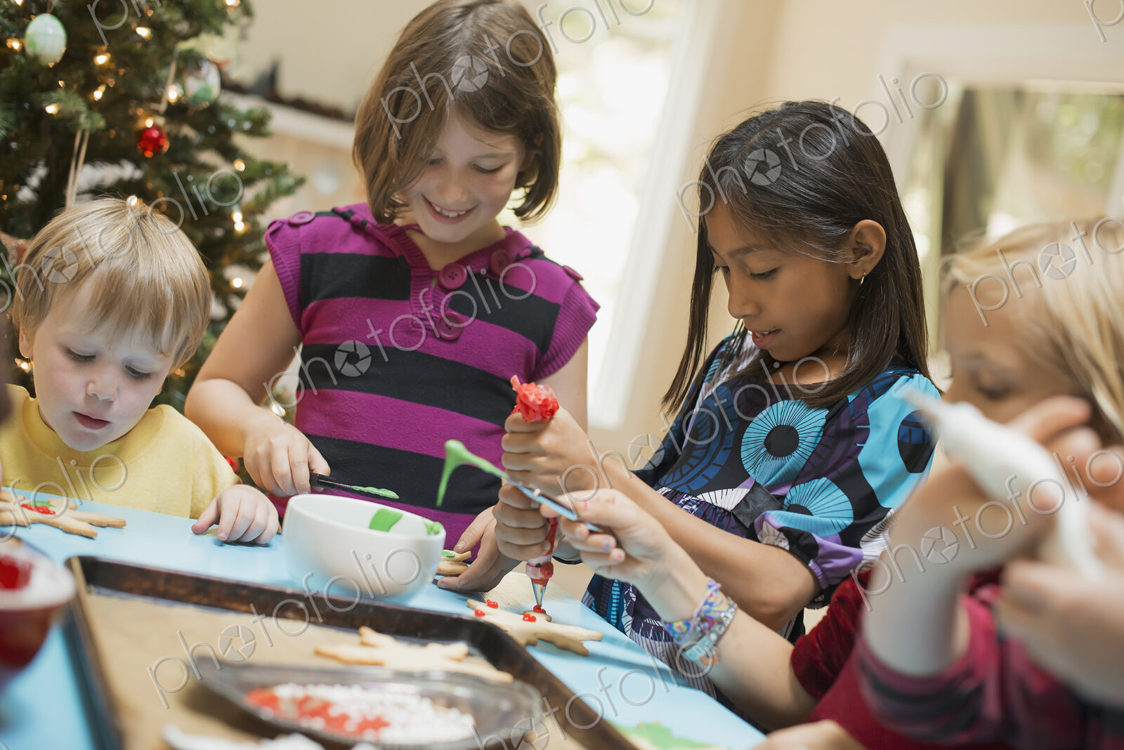 A group of children, girls and boys, around a table, decorating organic Christmas cookies.