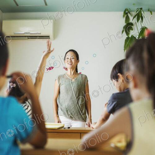 A group of children in a classroom, one with her hand up ready to answer a question.