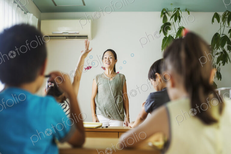 A group of children in a classroom, one with her hand up ready to answer a question.