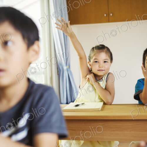 A group of children in a classroom, one with her hand up ready to answer a question. A group of children in a classroom, one with her hand up ready to answer a question.