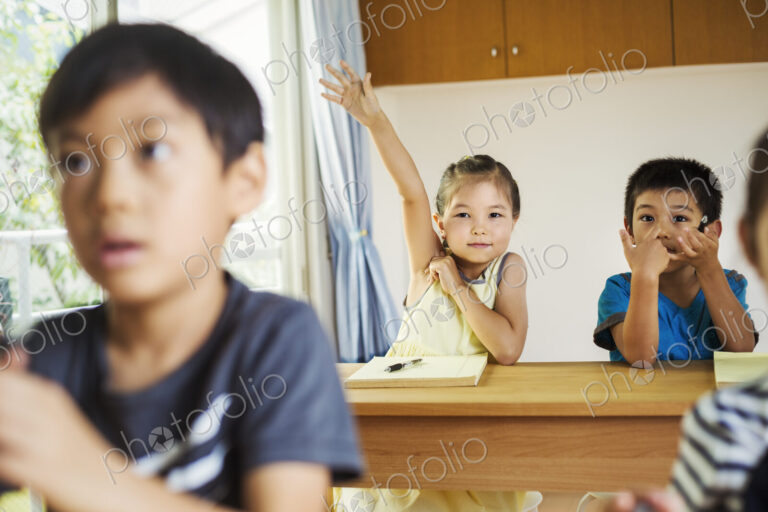 A group of children in a classroom, one with her hand up ready to answer a question.