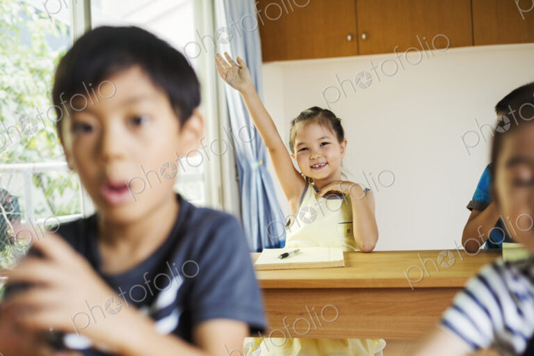 A group of children in a classroom, one with her hand up ready to answer a question.