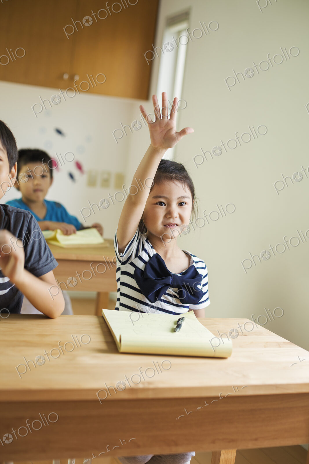 A group of children in a classroom, one with her hand up ready to answer a question.