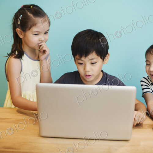 A group of children in school, three children sharing a laptop computer.