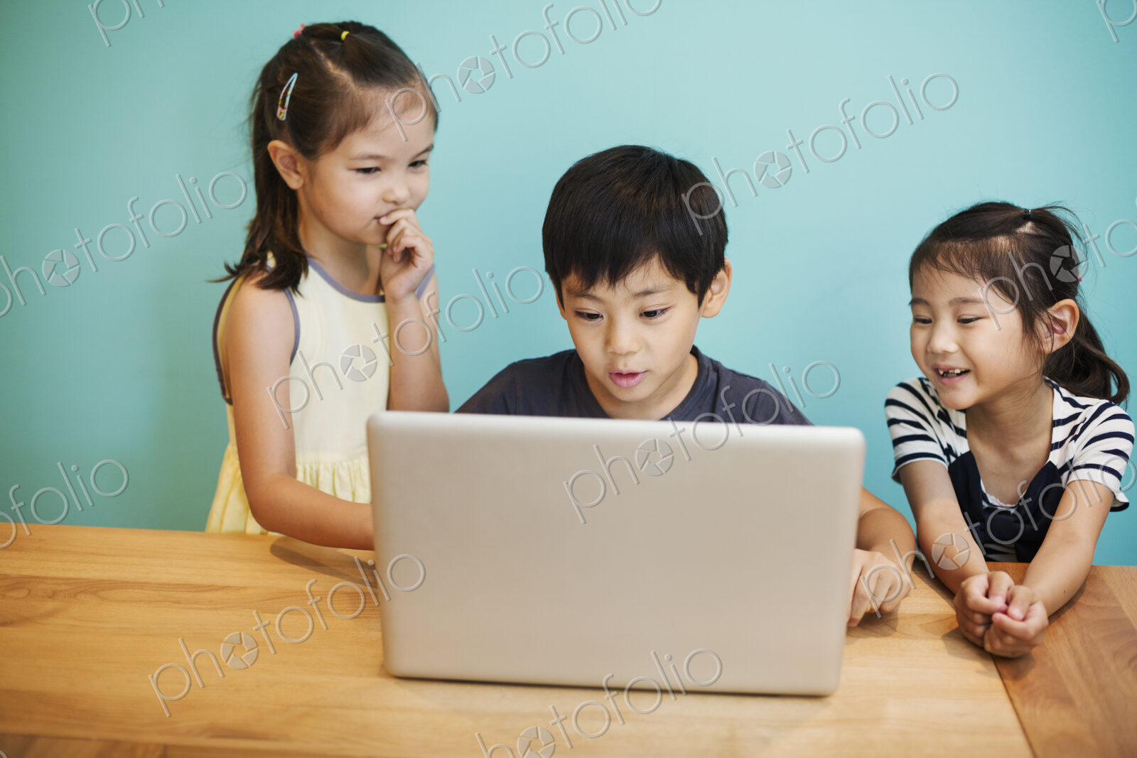 A group of children in school, three children sharing a laptop computer.