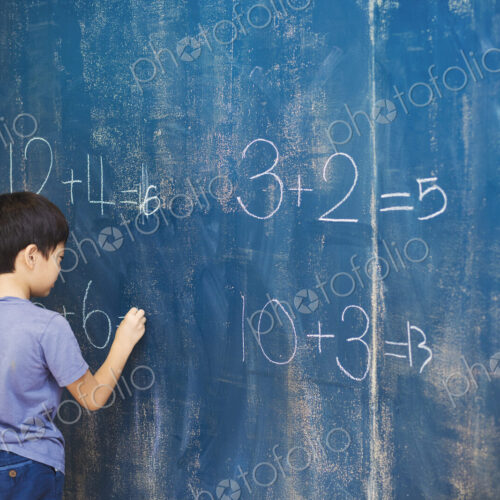 A group of children in school. A boy writing in chalk on a chalkboard. A group of children in school. A boy writing in chalk on a chalkboard.