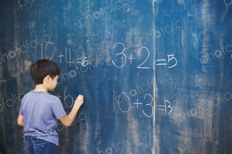 A group of children in school. A boy writing in chalk on a chalkboard.