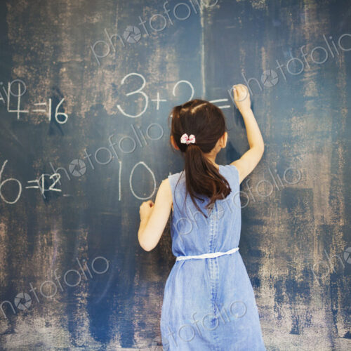 A group of children in school. A girl writing in chalk on a chalkboard. A group of children in school. A girl writing in chalk on a chalkboard.