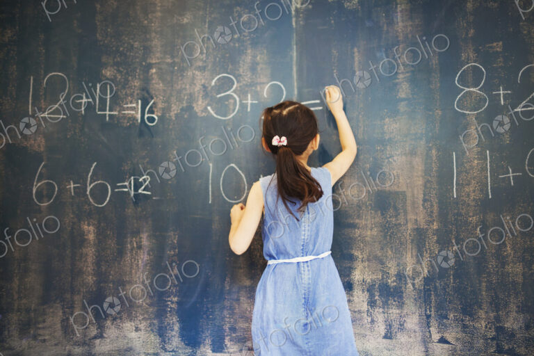 A group of children in school. A girl writing in chalk on a chalkboard.